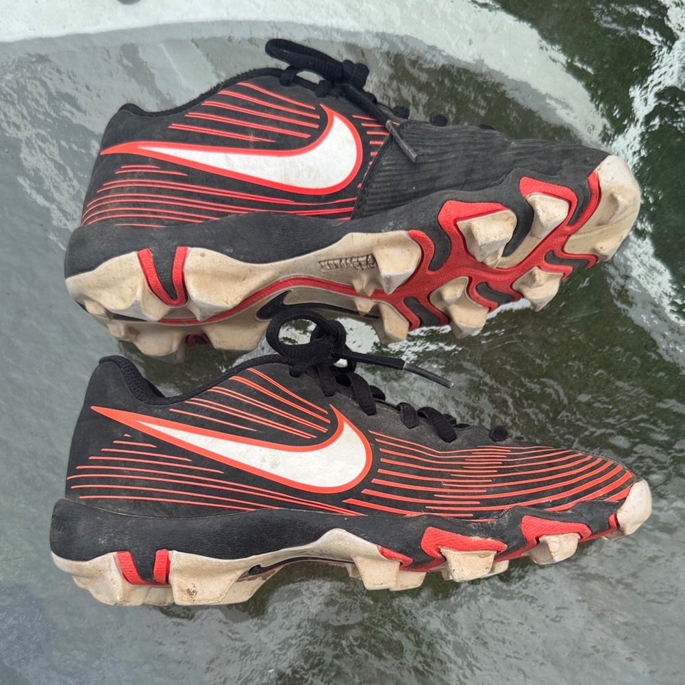 Nike Kids Black and orangish pink softball cleats.